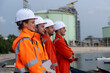 © Freeday photo - Workers observe operations at a coastal industrial site wearing safety gear and standing near water in the afternoon
