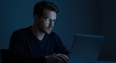 Man wearing glasses uses a laptop in a dark room at night.