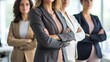 © Mey - Four businesswomen standing in a modern office with their arms crossed, wearing professional attire.
