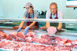 © JackF - Focused skilled workers of butchery shop, elderly man and young woman, working together behind counter, arranging fresh raw meat cuts in glass refrigerated showcase