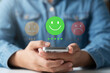 © Thapana_Studio - Customer experience rating concept showing hand holding smartphone with positive feedback emoji, satisfaction level, and review system for business or service analysis.