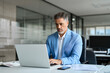 © insta_photos - 50 years old businessman executive investor, busy middle aged mature professional business man ceo wearing suit using laptop computer working on finance investment sitting at desk in corporate office.