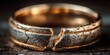 © Anca - Broken Wedding Band: Close-up view of a broken gold wedding band, signifying the end of a relationship or the fragility of commitment. The texture of the metal is rough and aged.