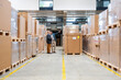 © Westend61 - Two employees having a meeting in a warehouse surrounded by cardboard boxes