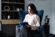 © Andrii Zastrozhnov - Young caucasian female adult writing in notebook while sitting in modern chair