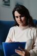 © Andrii Zastrozhnov - Caucasian female adult relaxing at home writing on blue clipboard