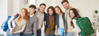 © Studio Romantic - Group portrait of happy smiling students standing together in classroom and hugging each other. Cheerful young people carrying backpacks and notebooks, looking at camera, ready for learning. Banner.