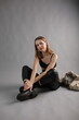 © Anhelina  - Young woman in a black crop top and leather pants sitting on the studio floor against a gray background. Stylish street-style outfit with a confident look.