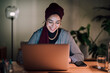 © Studio Marmellata - A young Moroccan Arab Muslim woman smiles while working on her laptop at a desk. She is focused and engaged with her work in a home office setting.