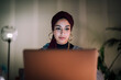 © Studio Marmellata - A young Moroccan Arab Muslim woman is focused on her laptop screen while working or studying indoors at night. She concentrates intently on the task.