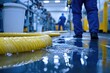 © Hutan - Industrial facility floor with water spill and cleaning equipment.  A wet factory floor,  with a worker in blue uniform. Yellow hoses for cleaning lie on the water