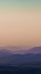 Wall Mural - Serene sunset landscape view with soft hues over layered rolling hills and distant mountains under a calm sky, creating a peaceful atmosphere for relaxation