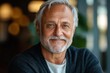 © Ulyana - Smiling elderly man with gray hair and beard wearing a dark sweater looking warmly at the camera in a softly lit indoor setting