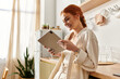 © LIGHTFIELD STUDIOS - Beautiful woman with red hair enjoys a quiet moment while using a tablet in a sunlit kitchen