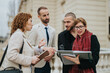 © qunica.com - Four colleagues discussing and collaborating in an outdoor setting near a modern building, exuding teamwork, professionalism, and communication.