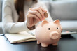 © Pormezz - Young woman saving money monthly expenses putting coin in to piggy bank on the table.