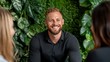 © Raul - Smiling Man is sitting and talking with two other people in front of a living green plant wall backdrop.