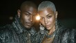 © Blackmint Studio - A hip hop couple poses confidently in matching silver and black outfits, adorned with jewelry, exuding style at a vibrant night event in the city