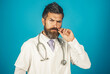 © Svitlana - Serious doctor man with beard and mustache in medical gown with stethoscope in hospital. Healthcare, clinic, medicine, treatment and medical staff. Bearded physician in white uniform with stethoscope.