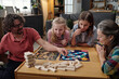 © pressmaster - Family sitting at table playing board game, with three children and two adults concentrating on the game, socializing and enjoying bonding moment