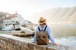 © maxbelchenko - Beautiful female traveler in a hat and with a backpack enjoying the seascape at sunset. Young woman with a backpack admiring the view of the bay. Travel and tourism concept. Active lifestyle.