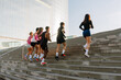 © Drobot Dean - A multinational group of young people running up concrete stairs outside a modern building on a sunny day, wearing athletic clothing, exercising together as part of an outdoor training session.