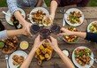 © Ozz - Friends enjoying a summer barbecue, toasting with wine around a table filled with food and salads.