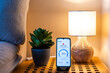 © Nanci - Home energy consumption monitoring app displaying high usage alert on smartphone placed on nightstand next to a lit lamp and a plant, promoting energy saving awareness and smart home technology