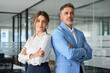 © insta_photos - Team portrait of two confident professional mature middle aged business man and business woman corporate executive leaders company managers standing in office arms crossed looking at camera.
