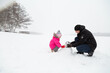 © Mariia - Father with daughter dressed warmly and in warm gloves builds a snowman in a snowy near the lake.