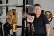 © Mdv Edwards - Happy Southeast Asian middle-aged man smiles while resting at a bench press station, holding a towel after finishing a gym set.
