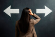© Who is Danny - Confused businesswoman looking at opposite arrows on dark background, symbolizing decision-making and direction choice concept.