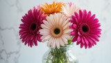 Gerbera daisies in a glass vase with pink orange and white flowers on a marble background surface