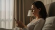 © Hamid - Young woman relaxing in bed in the morning light, using her smartphone and wireless earbuds for entertainment or communication