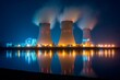 © Віталій Б. - Three cooling towers stand tall against the night sky, emitting steam while city lights shimmer on the water's surface, creating a serene yet industrial atmosphere