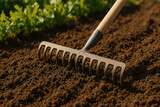 Gardening tool raking freshly prepared soil with greenery in background