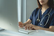 © tippapatt - Female doctor working on laptop computer at doctor's office. writing prescripstion, recording patient's information, healthcare and medicine concept
