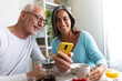 © Daniel - Happy mature caucasian married couple enjoying healthy breakfast at home looking at phone.