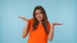 © kinomaster - Confused Woman in Orange Shirt Posing Against Blue Background