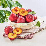 Świeże śliwki czerwone w drewnianym koszyczku na białym stole