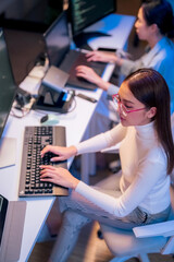 asian female programmer sits a dark tech workspace at night, fully focused on developing an online p