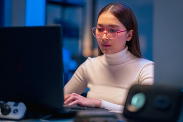 asian female programmer sits a dark tech workspace at night, fully focused on developing an online p