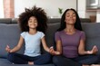 © Lens Wave - Cute little girl with young mother sitting in lotus pose on couch at home, mum and daughter practicing yoga and laughing, having fun on weekend