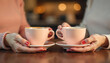 © Yasin - Close-up shot of two women's hands holding pink coffee cups at a cozy cafe setting.
