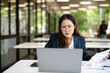 © maeching - Asian businesswoman working on financial market research using laptop and digital tablet, stressed about digital investment in office.
