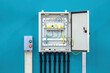 © Grispb - Open electrical distribution panel with circuit breakers, grounding wire, and control button box mounted on blue wall. Electrical engineering. Power control. Installation.
