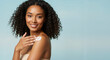 © Vasiliy - African American woman with curly hair applying moisturizer on shoulder against blue background. Natural skincare routine concept for beauty products, cosmetic advertising and summer skin protection
