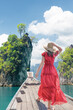 © Vladimir Razgulyaev - A woman elegantly dressed in a stunning red dress poses majestically against a gorgeous tropical island landscape