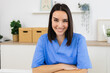 © Xavier Lorenzo - Smiling female nurse wearing blue uniform sitting at desk with arms crossed in bright doctor's office