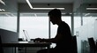 © meka - Silhouette of a concentrated professional using a laptop in a modern office